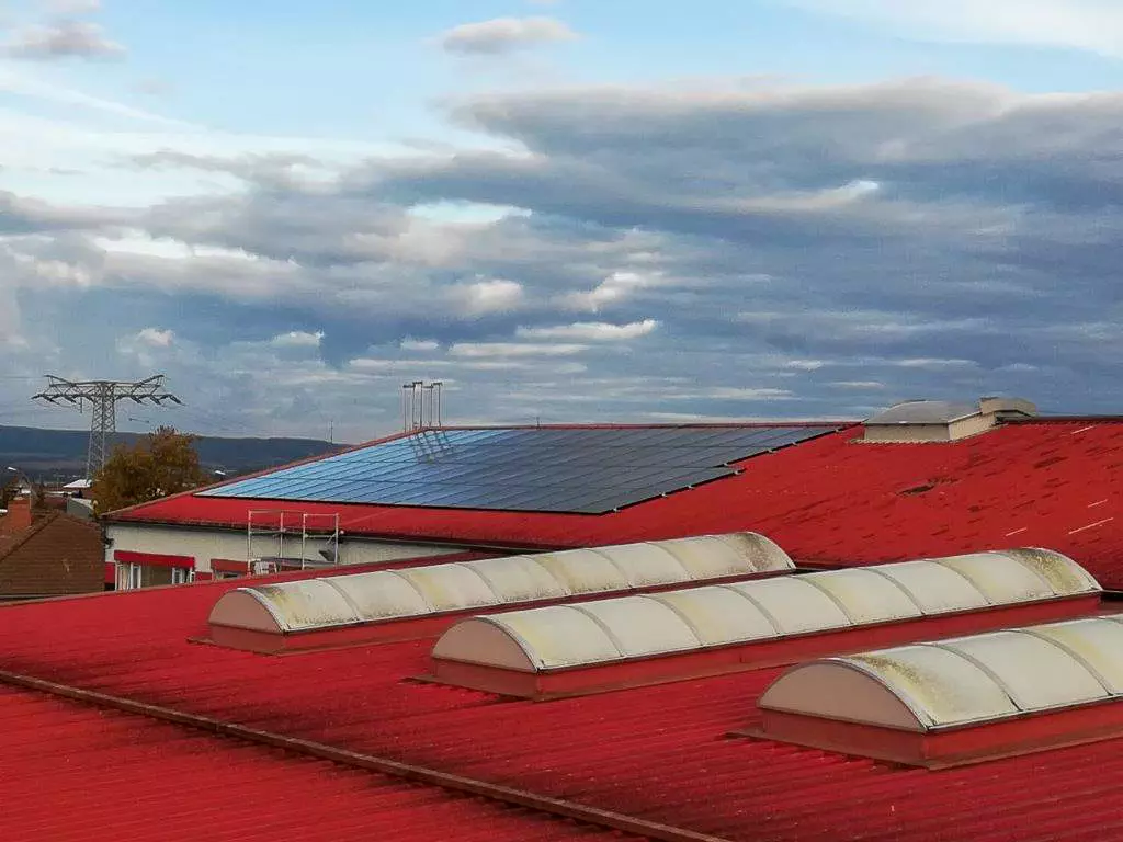 Rotes Dach mit Solaranlage bei bewölktem Himmel.